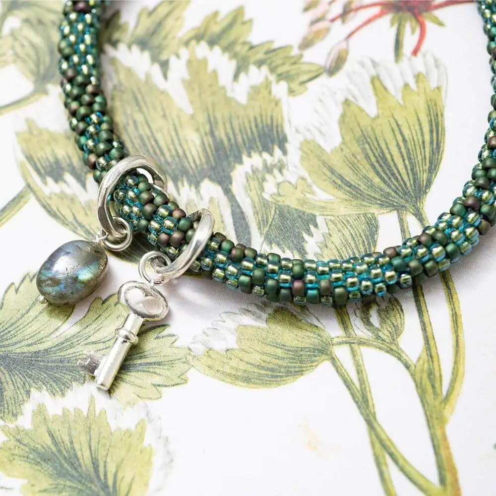 Rond gehaakte armband in licht en donker groen met een sleutelbedel en een labradoriet steen
