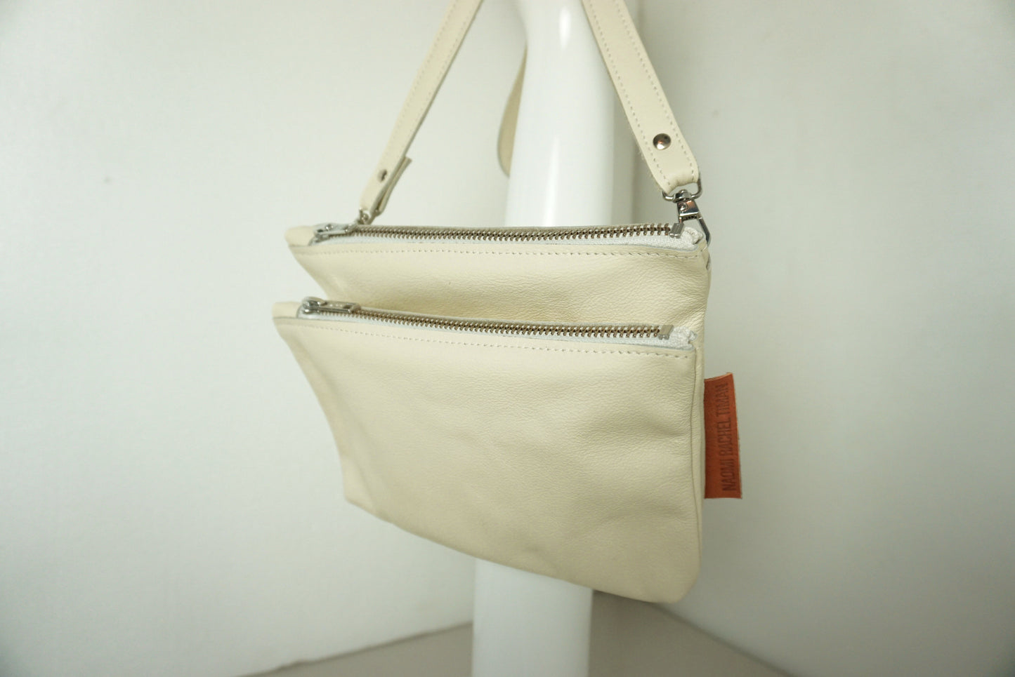 close up van Schoudertas van twee vakken die met drukknopen vast zitten met rits van creme gerecycled leer