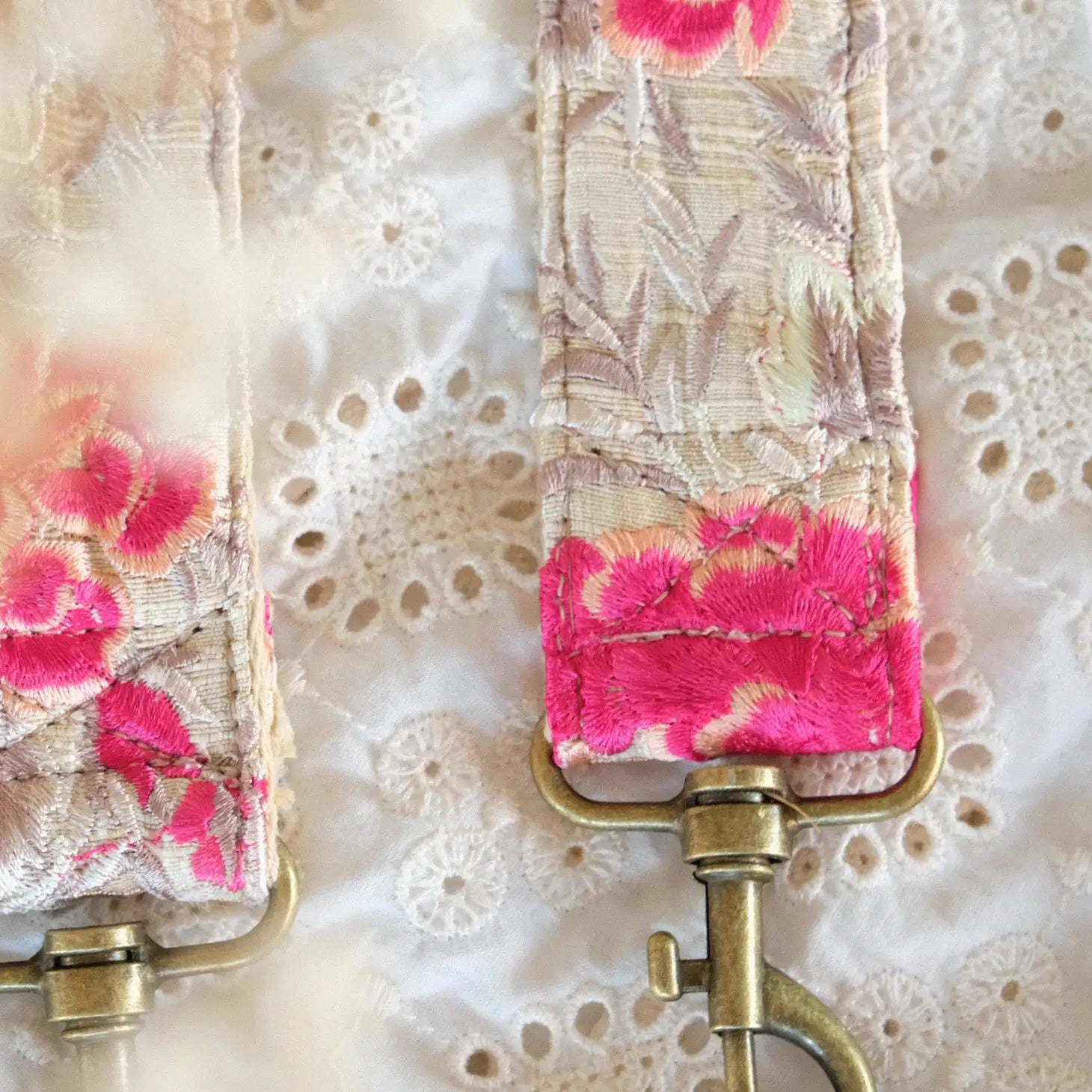 close up van telefoon/tasriem gemaakt van handgeborduurde witte en fushia bloemen op witte stof