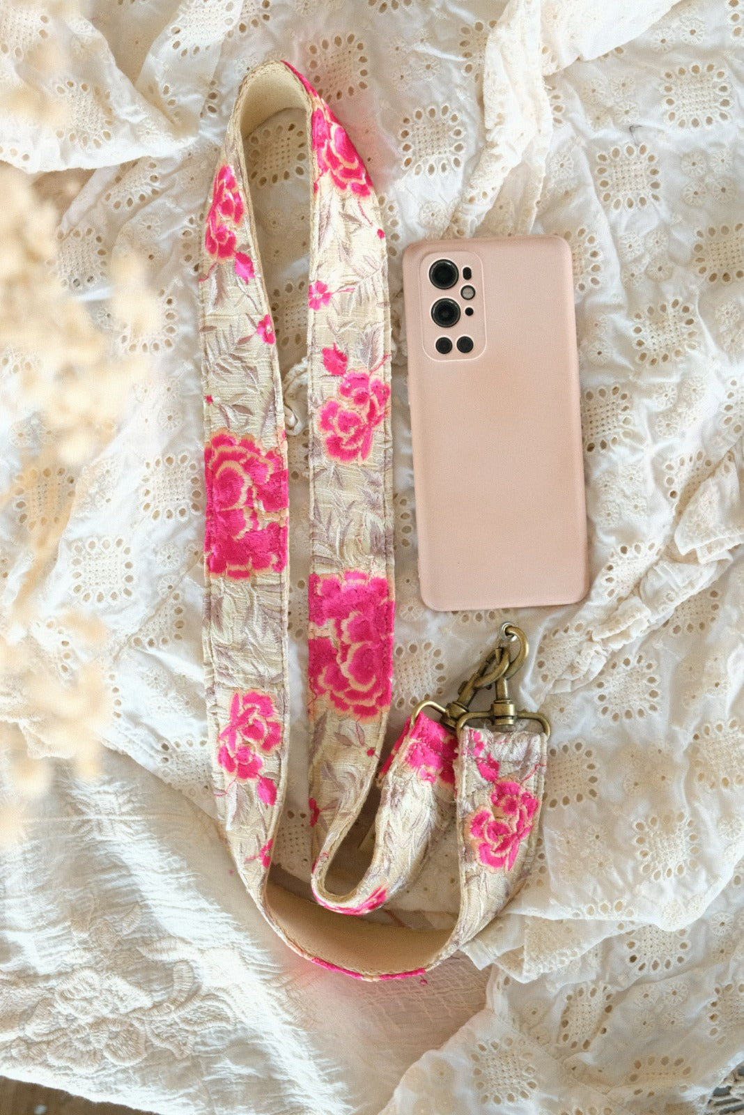 telefoon/tasriem gemaakt van handgeborduurde witte en fushia bloemen op witte stof aan telefoon vast gemaakt