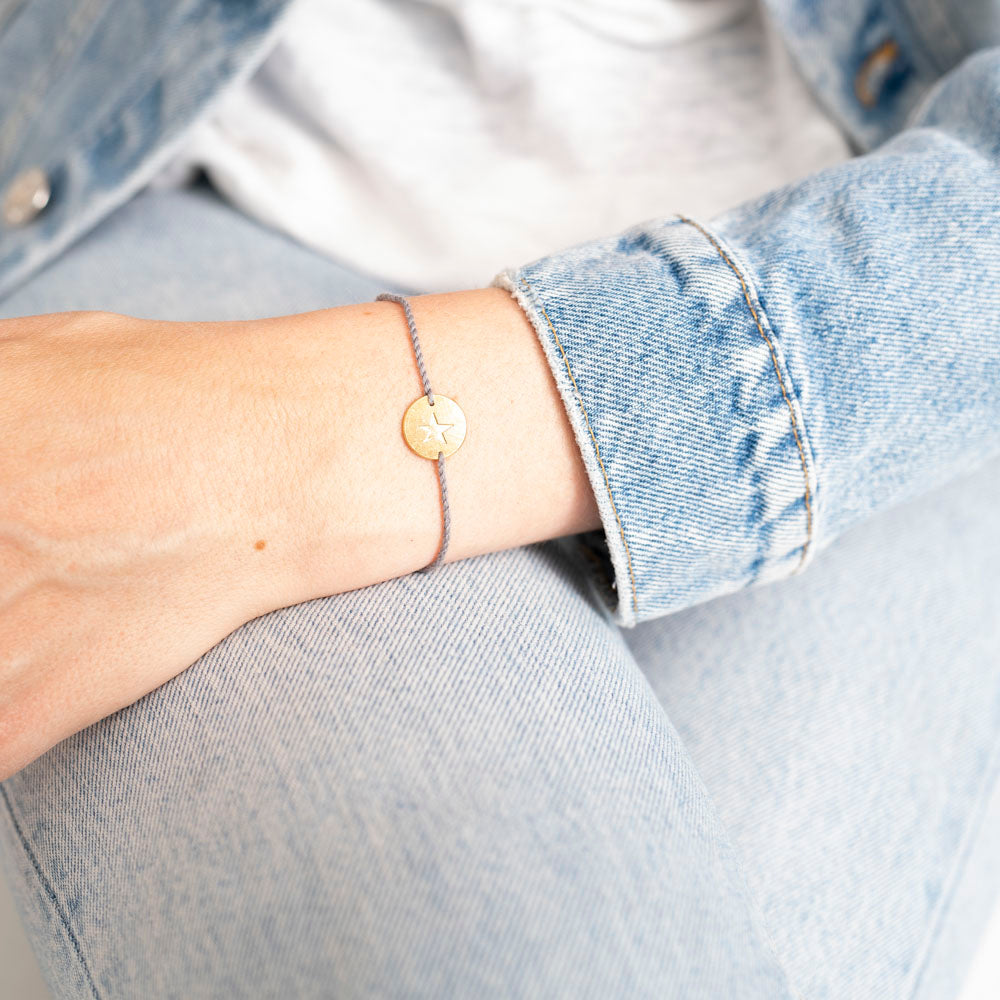 Klein kaartje met een waterverf afbeelding van een pauwenveer. Er zit een armbandje bij van grijs katoendraad met een goudkleurig muntje met een ster erop. De tekst is Proud of you.