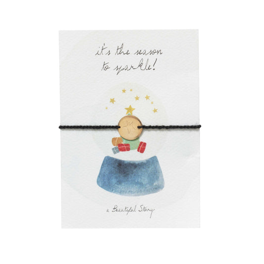 Klein kaartje met een waterverf afbeelding van een schudbol en de tekst It's the season to sparkle. Er zit een armbandje bij van zwart katoendraad en een goudkleurig muntje met een ster.