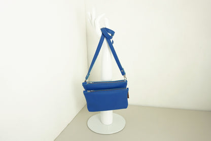 Kobaltblauwe Schoudertas van twee vakken die met drukknopen vast zitten met rits van gerecycled leer met schouderband op standaard