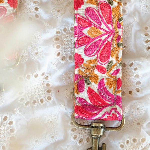 close up van telefoon/tasriem handgemaakt van witte stof met bloemen in meerdere kleuren roze en geel