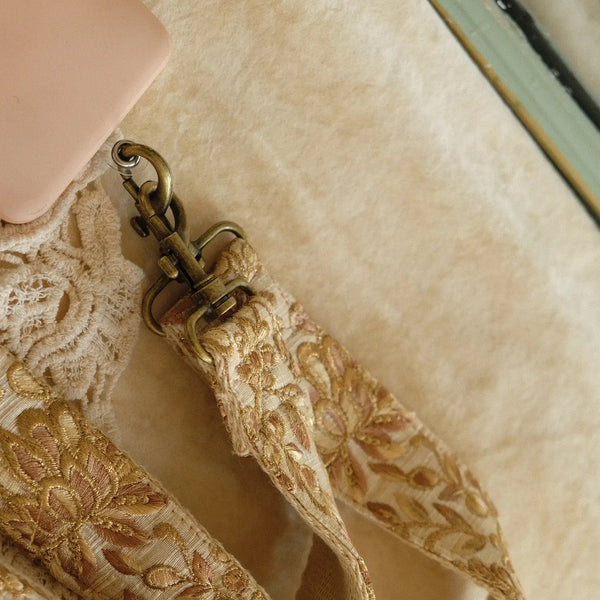 close upvan handgemaakte tas/telefoonriem van gouden bloemen op creme stof vastgemaakt aan telefoonhoesje